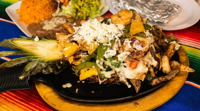 Sizzling fajitas with shrimp, chicken, peppers, and cheese served in a pineapple half.