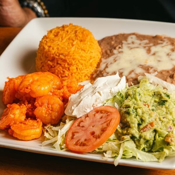 A plate of Mexican food with shrimp, rice, refried beans, guacamole, and sour cream.