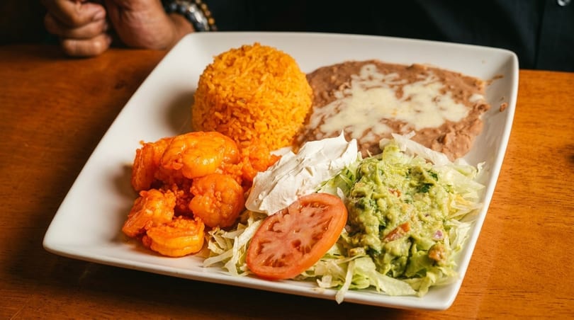 A plate of Mexican food with shrimp, rice, refried beans, guacamole, and sour cream.