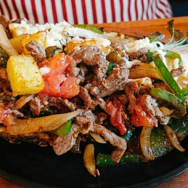 Sizzling fajitas with steak, peppers, onions, pineapple, and cheese served in a pineapple half.